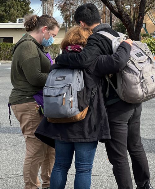 Rear view of two people embracing while a third talks to them.